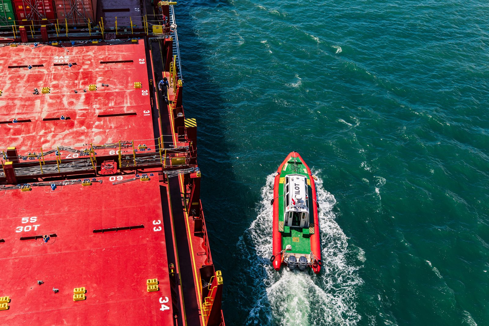 A pilot boat alongside the red deck of a container ship