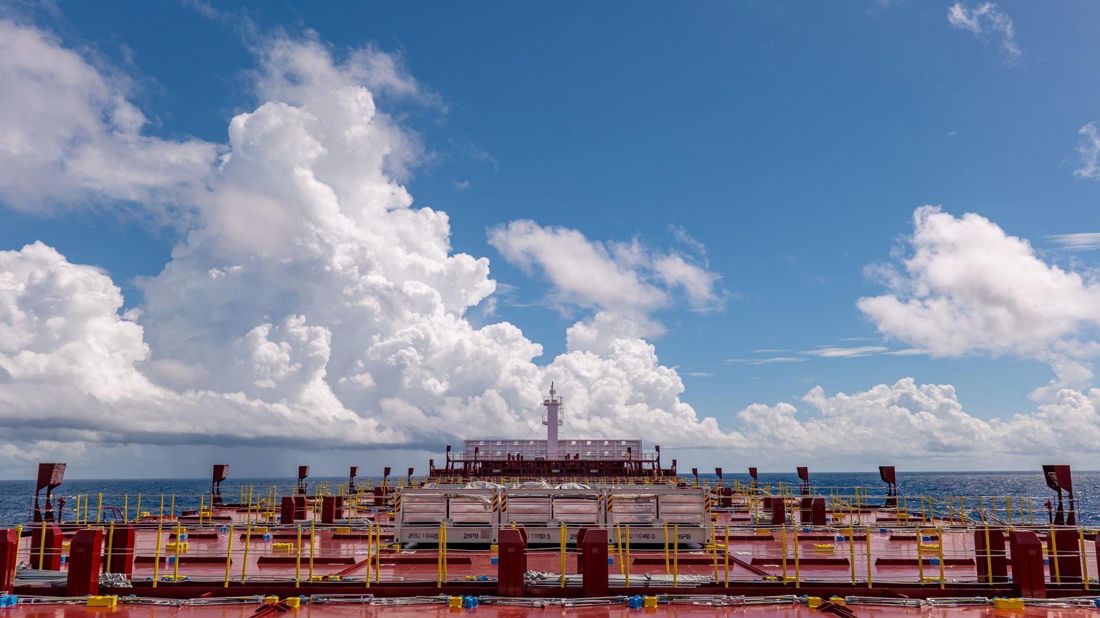 Container ship deck beneath cumulus clouds